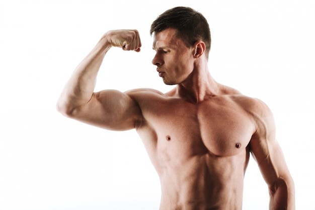 Close-up portrait of young muscular man with short haircut looking at his triceps