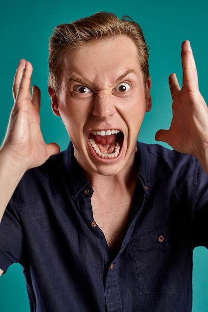 Close-up portrait of a young nice ginger fellow in a stylish navy t-shirt looking mad while posing on blue studio background. Human facial expressions. Sincere emotions concept. Copy space.