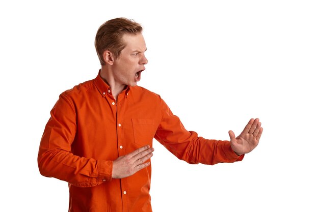 Крупным планом портрет молодого симпатичного рыжего парня в стильной оранжевой рубашке, который ведет себя так, будто борется, позируя изолированно на белом студийном фоне. Выражение лица человека. Концепция искренних эмоций