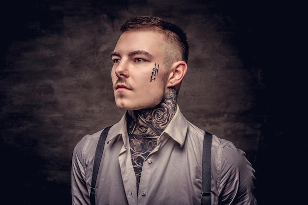 Free photo close-up portrait of a young old-fashioned tattooed guy wearing white shirt and suspenders. isolated on a dark background.
