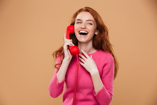 Close up portrait of a young pretty redhead girl talking by classic red phone