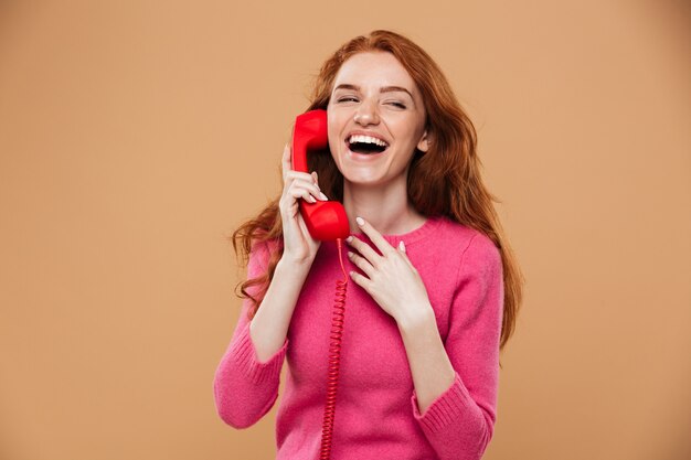 Крупным планом портрет молодой довольно рыжая девушка разговаривает по классическим красным телефоном