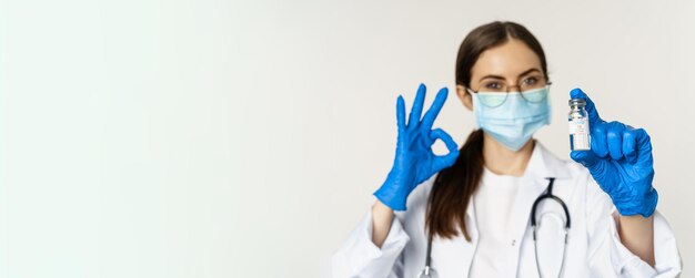 Close up portrait of young professional woman doctor physician in medical face mask and glasses show