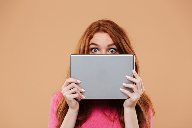 Close up portrait of a young redhead girl covering face with digital tablet