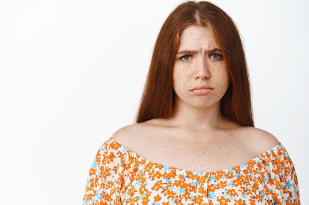 Free photo close up portrait of young redhead girl grimacing disappointed frowning and looking upset offended by smth standing over white background