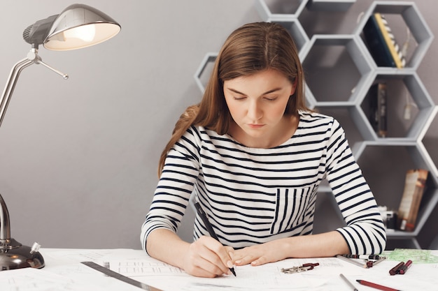 Free photo close up portrait of young serious architect girl doing her work in cosy coworking space, looking at paper with serious and unhappy expression.