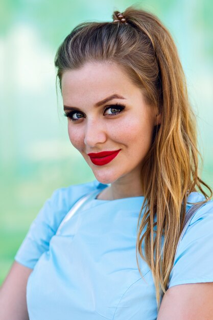 Close up portrait of young smelling blonde woman, ponytail bright make up, positive mood, cute elegant blue dress