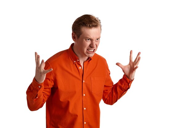 Close-up portrait of a young stately ginger male in a stylish orange shirt acting like he is beside himself with rage while posing isolated on white studio background. Human facial expressions. Sincer