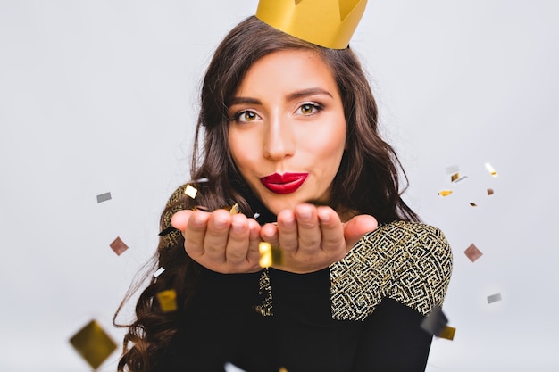 Close up portrait young stylish woman celebrating new year, wearing black dress and yellow crown, happy carnival disco party, sparkling confetti