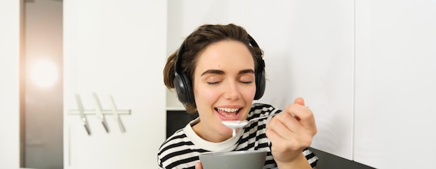 Free photo close up portrait of young woman enjoys eating her breakfast having cereals with milk holding spoon