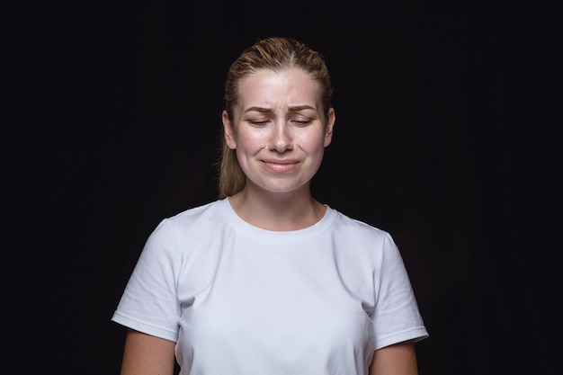 Free photo close up portrait of young woman isolated on black studio background. photoshot of real emotions of female model. crying with closed eyes, sad and hopeless. facial expression, human emotions concept.