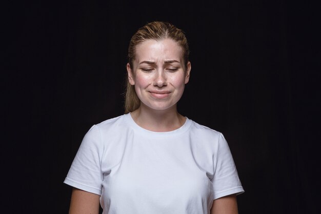 Close up portrait of young woman isolated on black studio background. Photoshot of real emotions of female model. Crying with closed eyes, sad and hopeless. Facial expression, human emotions concept.