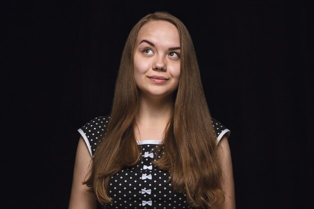 Close up portrait of young woman isolated on black studio background. Photoshot of real emotions of female model. Dreaming and smiling, hopeful and happy. Facial expression, human emotions concept.