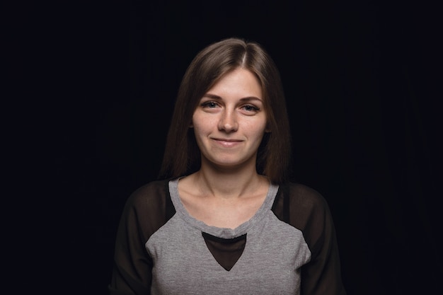 Close up portrait of young woman isolated on black studio background. Photoshot of real emotions of female model. Smiling, feeling happy. Facial expression, pure and clear human emotions concept.