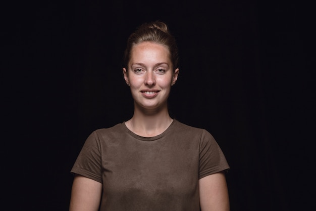 Close up portrait of young woman isolated on black studio background. Smiling, feeling happy.