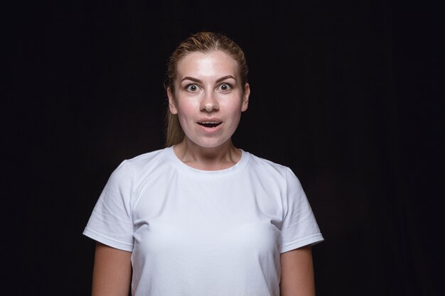 Close up portrait of young woman isolated on black studio background. Wondering, exciting and astonished.