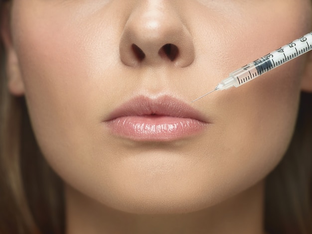 Close-up portrait of young woman on white studio wall. Filling surgery procedure. Lip augmentation.