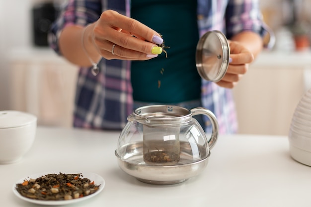 Primo piano di versare erbe aromatiche in teiera per preparare il tè al mattino per colazione