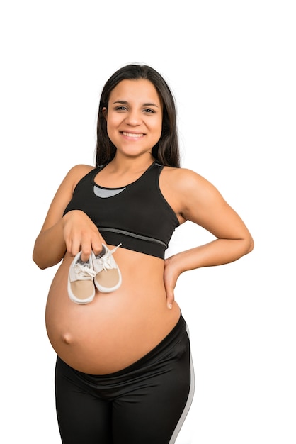 腹に赤ちゃんの靴を保持している妊婦のクローズアップ