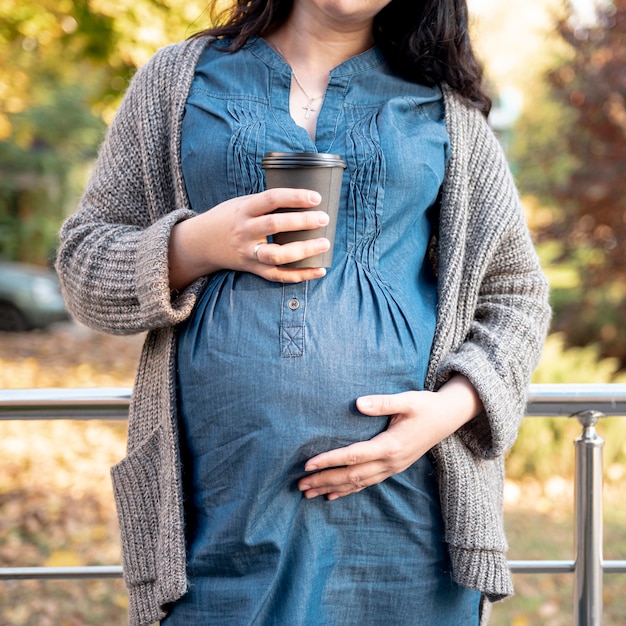 コーヒーのカップを保持しているクローズアップの妊娠中の女性