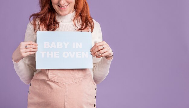 Close-up pregnant woman holding paper with baby in the oven message