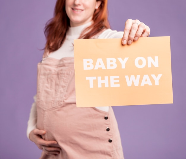 Close-up pregnant woman holding paper with baby on the way message