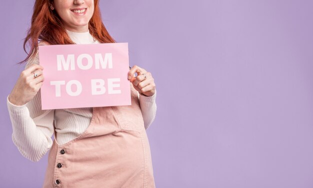 Close-up pregnant woman  holding paper with mom to be message