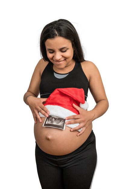 Close-up of pregnant woman holding the picture of the ultrasound scan of baby and with santa hat