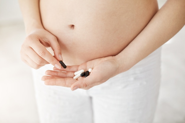 Крупным планом беременная женщина, держащая рецептурные таблетки, страдающих тошнотой или аллергией. Концепция здоровой беременности.