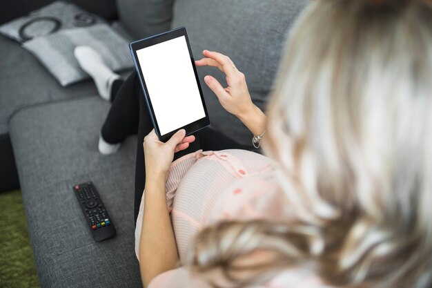 Крупный план беременная женщина с помощью цифрового планшета с пустым белым экраном