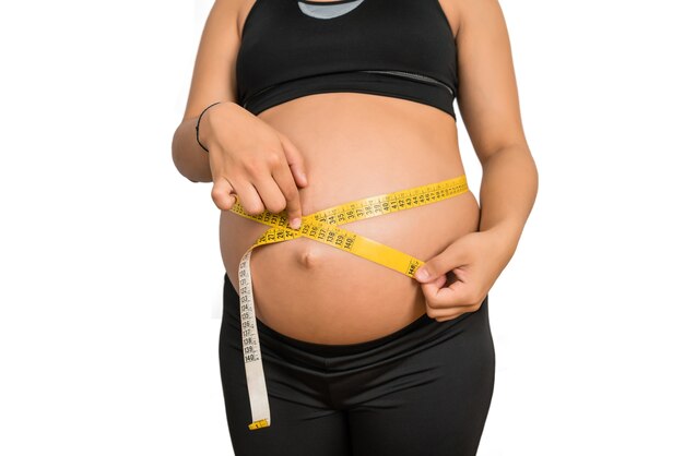 Close-up of pregnant woman using measuring tape to check baby development