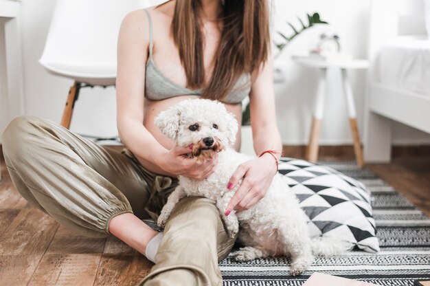 Close-up of pregnant woman with her lovely white toy poodle sitting on floor