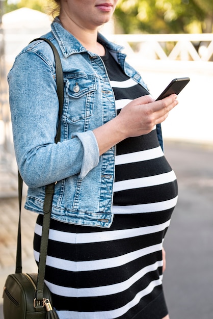 Close-up pregnant woman with smartphone outdoors