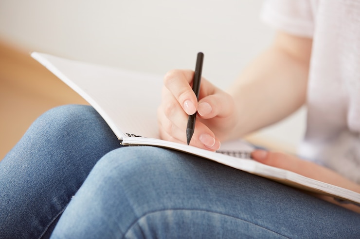 Free Photo close up of pretty young teenage girl sitting on her floor and making notes to her diary