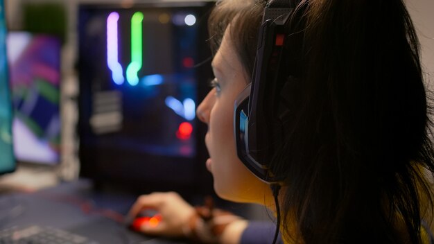 Close-up of pro gamer talking with friends on networks for space shooter virtual competition. Competitive woman with headphones streaming online cyber performing during gaming tournament