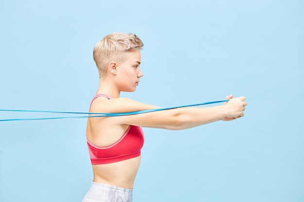 Free photo close up profile image of self determined healthy young short haired woman in sports clothes using resistance band to strengthen upper body. healthy active lifestyle, energy and motivation concept