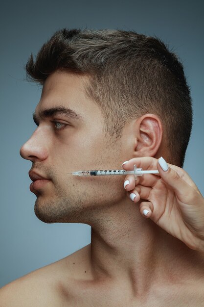 Close-up profile portrait of young man isolated on grey studio background. Filling surgery procedure. Concept of men's health and beauty, cosmetology, self-care, body and skin care. Anti-aging.