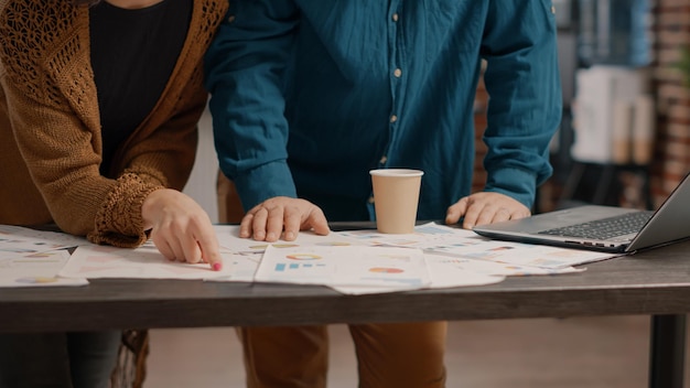 Close up of rate charts papers with analysis information on desk. Man and woman looking at files to plan project and presentation in startup office. Colleagues doing teamwork for strategy