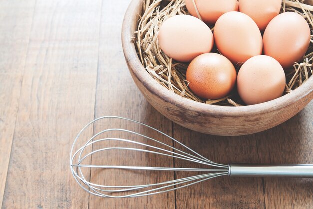 Close-up of raw chicken eggs in wooden bowl on wood background with kitchen utensil