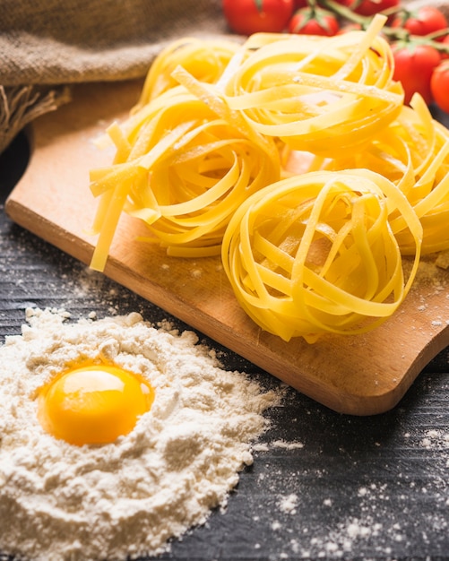 Close-up of raw tagliatelle on chopping board with egg york in flour