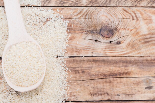 Close-up of raw white rice in spoon over textured plank