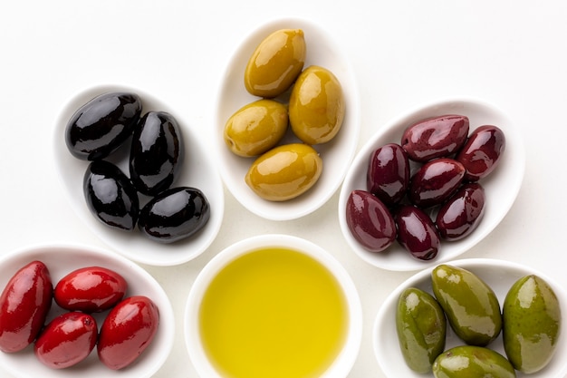 Close up red black yellow purple olives on plates with leaves and olive saucer