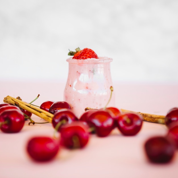 Close-up of red cherries with strawberry smoothie on pink desk