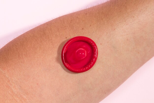 Close-up red condom on person's arm