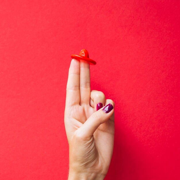Close-up red condom on woman's fingers 
