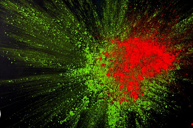 Close-up of red and green holi color exploding on dark background
