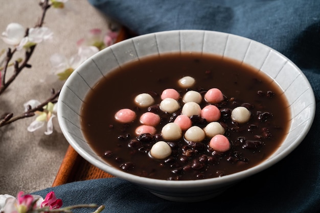 Close up of red and white tangyuan (tang yuan, glutinous rice dumpling balls) with sweet red bean soup in a bowl on gray table background for winter solstice festival food.