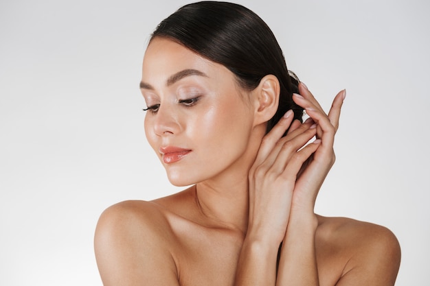 Close up of relaxed brunette woman with clean skin posing at camera with closed eyes, isolated over white