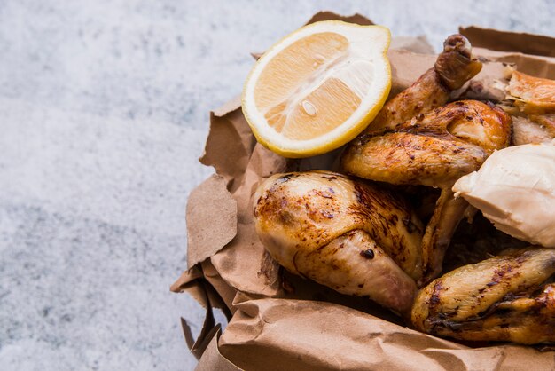 Close-up of roasted chicken and lemon slice in brown paper