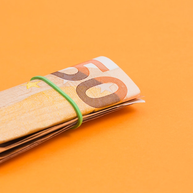 Free photo close-up of rolled up euro note tied with rubber on an orange backdrop